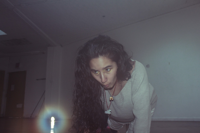 A person with long brown hair crawls towards a light on the floor. 
